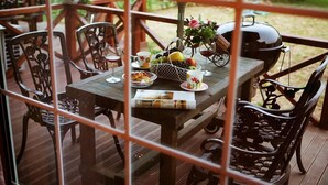 An outdoor dining area with a wooden table set for two, surrounded by intricately carved chairs. A basket of fruits and a grill are also visible. - Popcorn House Pension (Gapyeong)