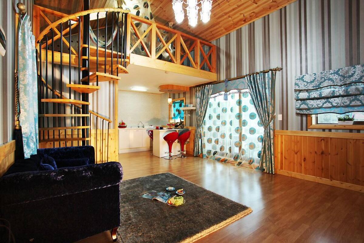 Habitación estilo loft con escalera de madera, cocina y un rincón de descanso acogedor con sofá oscuro y alfombra.