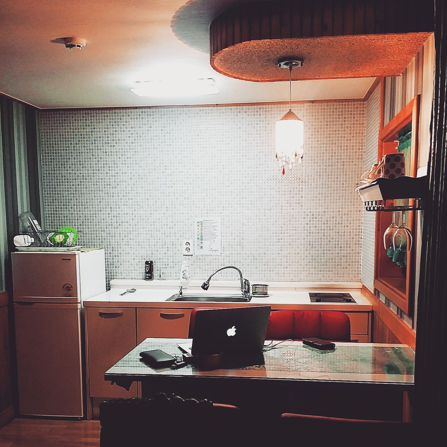 A compact kitchen with a white refrigerator, a sink, and a dining table with a laptop.