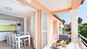 A modern kitchen with white cabinets and a green countertop, a dining area with white chairs and a table, and a balcony with a table set with food and drinks.