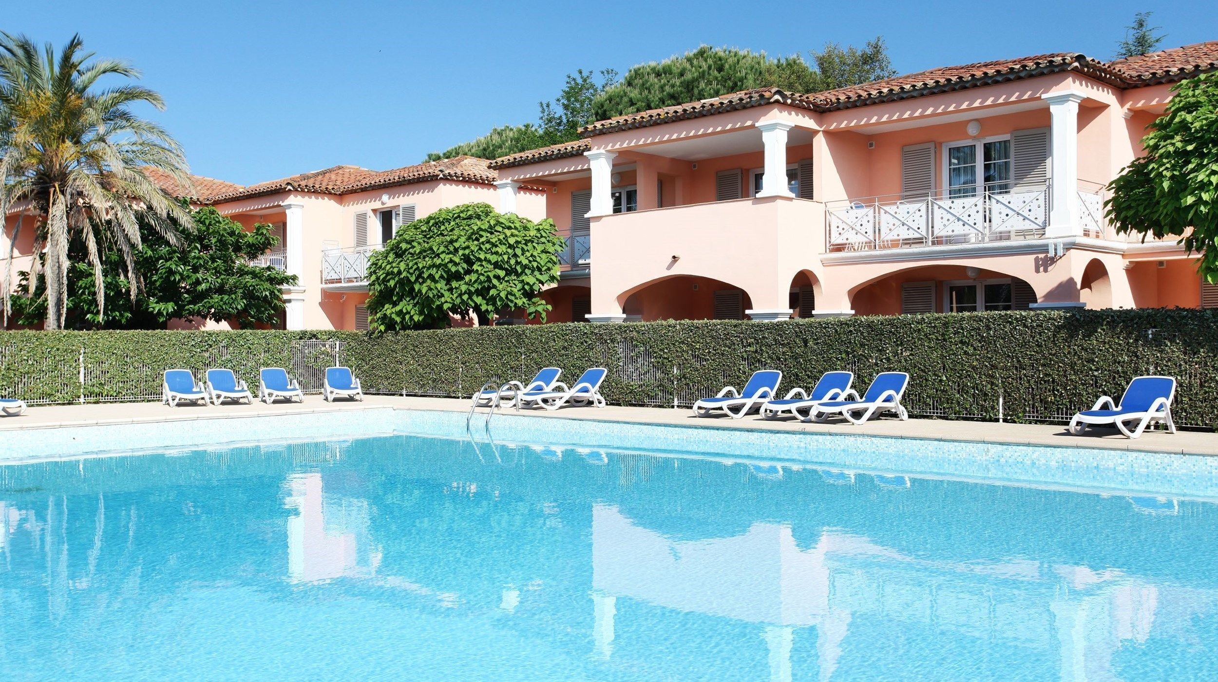 A swimming pool with lounge chairs and a building with a tiled roof and balconies.
