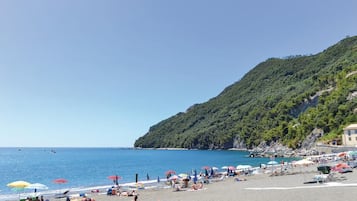 Una spiaggia con ombrelloni, persone che prendono il sole e una collina sullo sfondo.