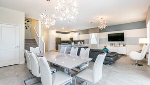 A modern kitchen with a built-in oven, a dining area with a white table and chairs, and a living area with a gray sofa and a TV mounted on the wall. - Champions Gate Exec Villas- 1686mvd (Davenport)