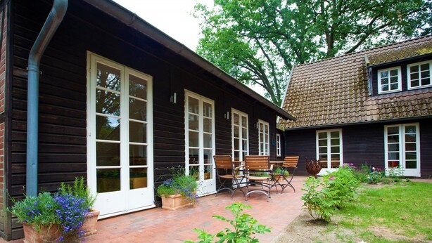 A wooden house with large windows and a brick patio. - Ferienhaus Fontane (Undeloh)