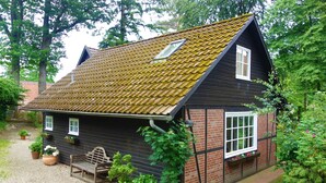 A traditional house with a sloped roof, a front porch with a bench, and potted plants around the entrance. - Ferienhaus Fontane (Undeloh)