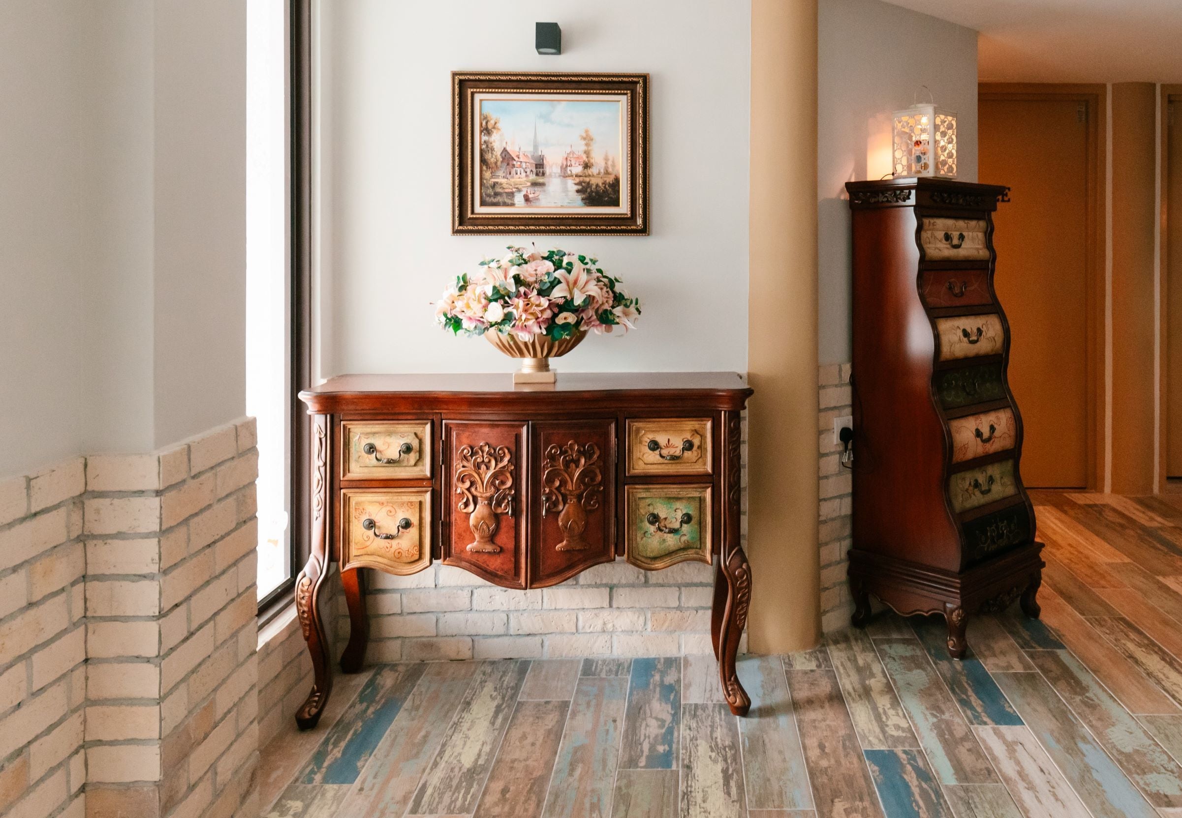 Una consola de madera con un florero, un cuadro enmarcado en la pared y un mueble de madera alto y ornamentado.