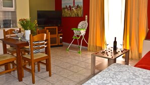 A living room with a TV, a dining table, chairs, a sofa, a small table with a bottle and glass, and a painting on the wall. - Steps from the beach, Near city centre,Angela apartment (Chania)
