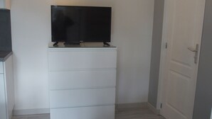 Ein Zimmer mit einem weißen Schminktisch, einem flachbildfernseher darauf, einer Wandleuchte und einer Tür.
