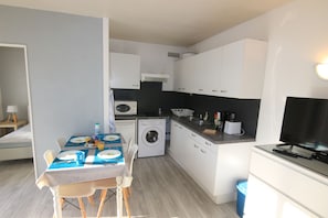 A compact kitchen with white cabinets, a washing machine, and a dining area with a table set for two.