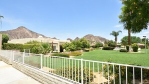 A residential area with a well-maintained lawn, a white fence, and a mountain range in the background.