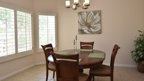 A dining room with a round table, four chairs, a chandelier, a large flower painting, and a potted plant.