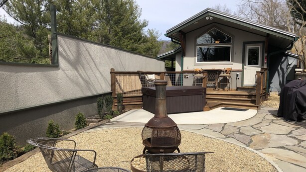 Une terrasse avec un sol en pierre, un barbecue en métal et deux chaises en métal.