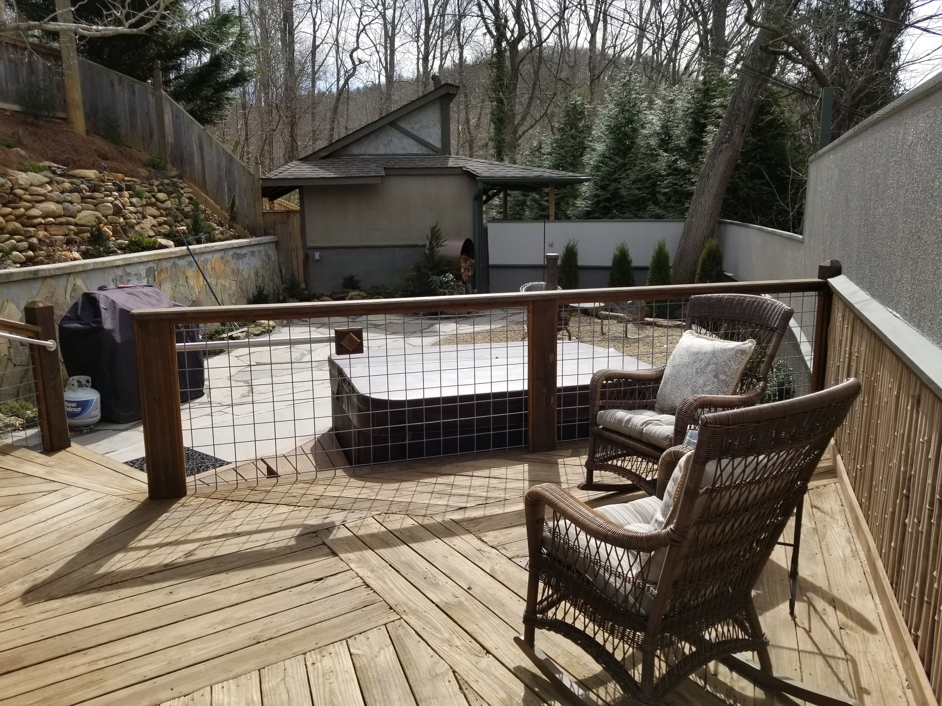 Une terrasse en bois avec un jacuzzi, des fauteuils en osier et un mur en pierre.