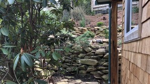 Un jardin avec un mur de pierre, une clôture en bois et un bâtiment en arrière-plan.
