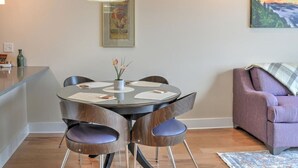 Un comedor con una mesa redonda, cuatro sillas, un florero con flores, un cuadro en la pared y un sofá púrpura.