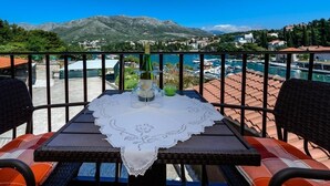 A balcony with a table set for two, overlooking a marina and mountains.