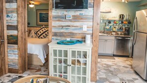 L’intérieur d’un chalet rustique comprend un lit, un petit meuble, un téléviseur et un coin cuisine avec un réfrigérateur et un évier.