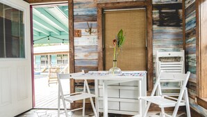 L’intérieur d’un chalet en bois, avec une table et des chaises blanches, une porte et une vue sur un espace extérieur.
