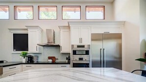 Une cuisine moderne avec des meubles blancs, un îlot en marbre et des appareils électroménagers intégrés, notamment un réfrigérateur, un four et un micro-ondes.