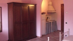 Een smalle gang met een houten garderobe en een keukenhoek, met een betegelde spatwand en geruit gordijn.