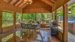 A covered outdoor deck with wooden flooring, a grill, and a dining area with chairs and a table. - Chalet Le Supérieur/Tremblant- Lac-Supérieur/Spa++ (Lac-Supérieur)