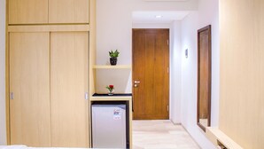 Quarto de hotel com armário de madeira, mini-frigorífico, porta de madeira e prateleira com uma planta e um vaso.