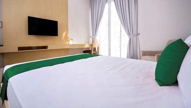 Quarto de hotel com uma cama grande, televisão de tela plana na parede e janela com cortinas.