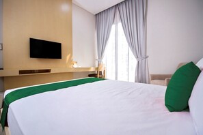 A hotel room with a large bed, a flat-screen TV mounted on the wall, and a window with curtains. - MK House SCBD (Jakarta)
