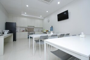 Une cuisine moderne avec des meubles blancs, un réfrigérateur noir et un coin repas doté de tables et de chaises blanches.