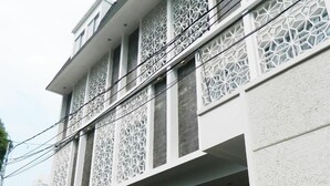 Um edifício moderno com fachada branca, janelas de treliça decorativas e entrada protegida por portão.