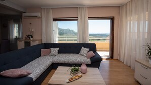 A modern living room with a sectional sofa, a coffee table, and a view of a mountainous landscape through large windows. - Holiday House App Grace with pool and view in Klis (Klis)