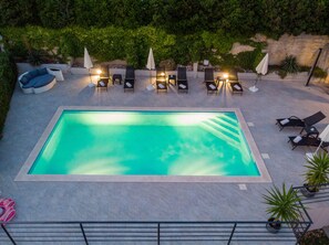 Uma piscina retangular com espreguiçadeiras e guarda-sóis dispostos ao redor.