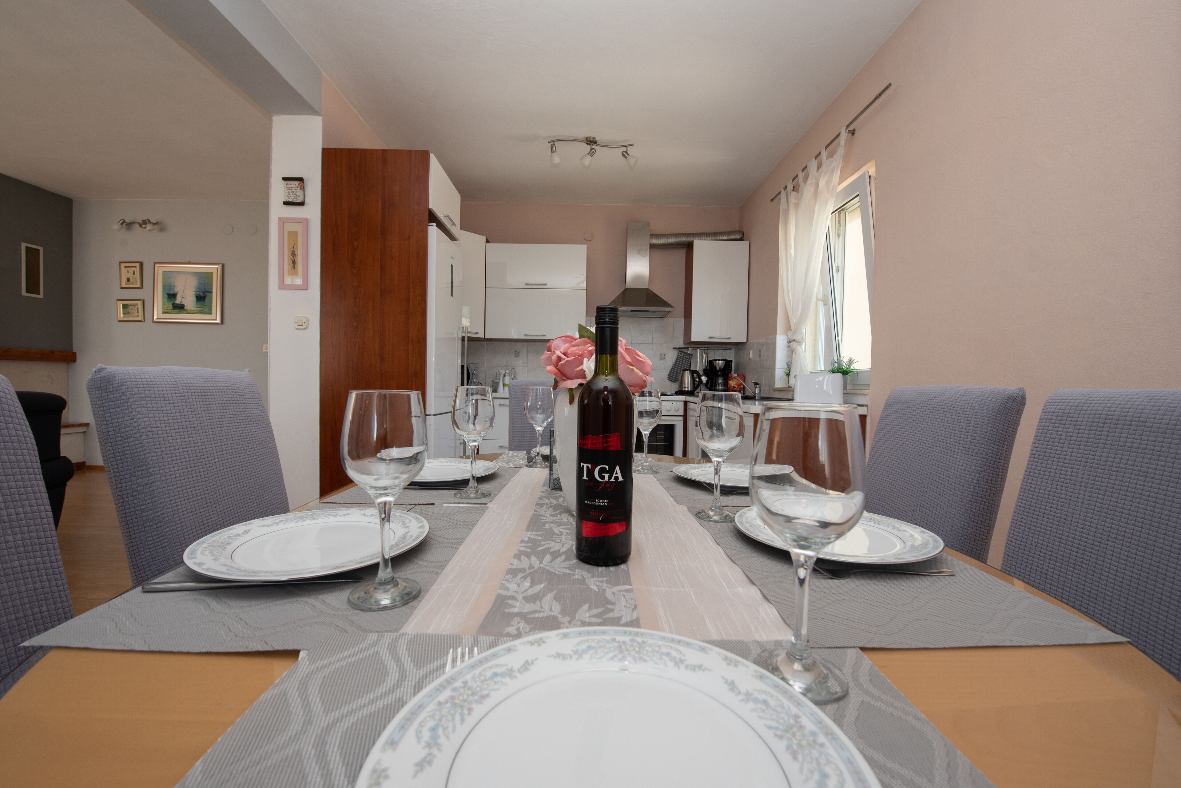 Un coin repas avec une table dressée pour quatre personnes, une bouteille de vin TGA et une cuisine en arrière-plan.