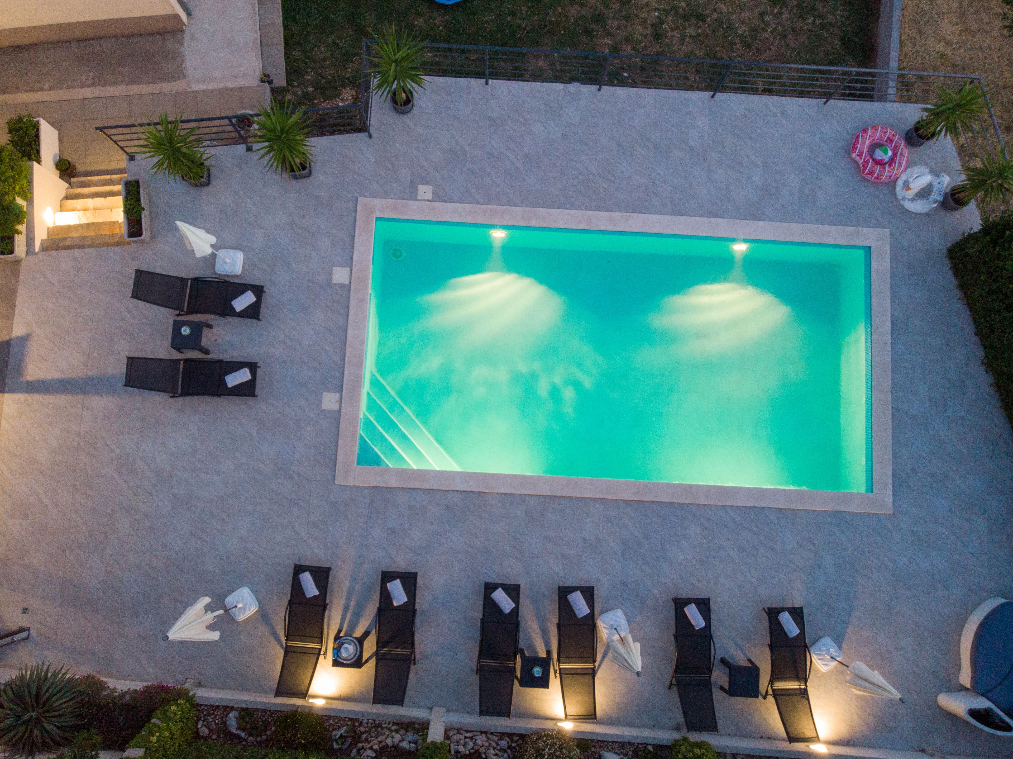 An aerial view of a swimming pool with lounge chairs and umbrellas, surrounded by potted plants.