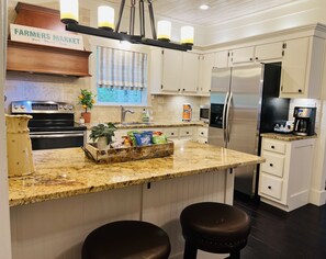 A kitchen with white cabinets, a stainless steel refrigerator, a coffee maker, and a wooden island with stools.