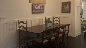 En matplats med ett träbord och stolar, en taklampa och skyltar som visar att det är ”Crosby Cottage” och ”Café Restaurant”.