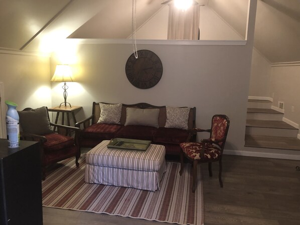 A living room with a sofa, armchair, ottoman, and a clock on the wall.