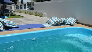 Una piscina pequeña al aire libre con sillones de descanso y almohadones a rayas.