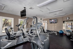 A gym with various exercise equipment, a television, and a clock on the wall.