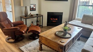Een woonkamer met een leren fauteuil, een houten salontafel, een bank, een open haard en een aan de muur bevestigde televisie.