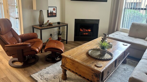 Una sala de estar con un sillón de cuero, una mesa de centro de madera, un sofá, una chimenea y un televisor montado en la pared.