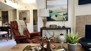 Een woonkamer met een bruine leren fauteuil, een houten salontafel en twee bronzen hertenbeeldjes.