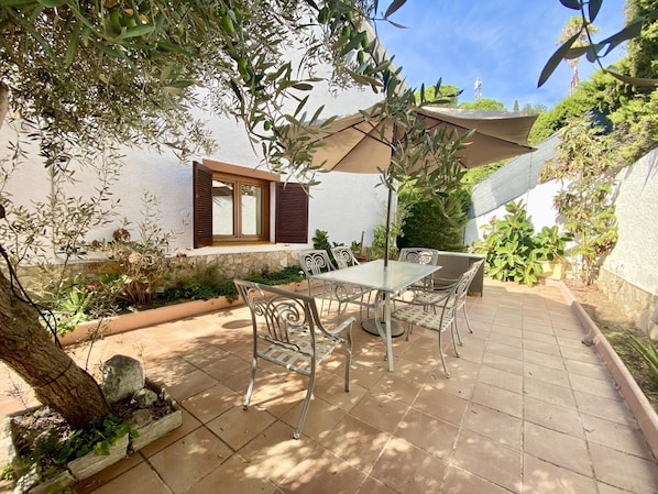 Une terrasse avec une table et des chaises, entourée de plantes et agrémentée d’une pergola.