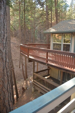 A wooden deck with railings, a small building with a sloped roof, and a forested background. - Spacious, bright, cozy, single floor home nestled in pine trees (Groveland)