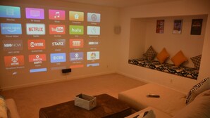 A living room with a large screen displaying various streaming services. There is a sofa, a coffee table, and a remote control on the coffee table. - Spacious, bright, cozy, single floor home nestled in pine trees (Groveland)
