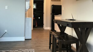 A modern kitchen with a dining area, a TV mounted on the wall, and a sign that says "Friends Gather Here". - Modern Tiny House in Apple Orchard w/Mountain View! Between Zion and Bryce (Glendale)
