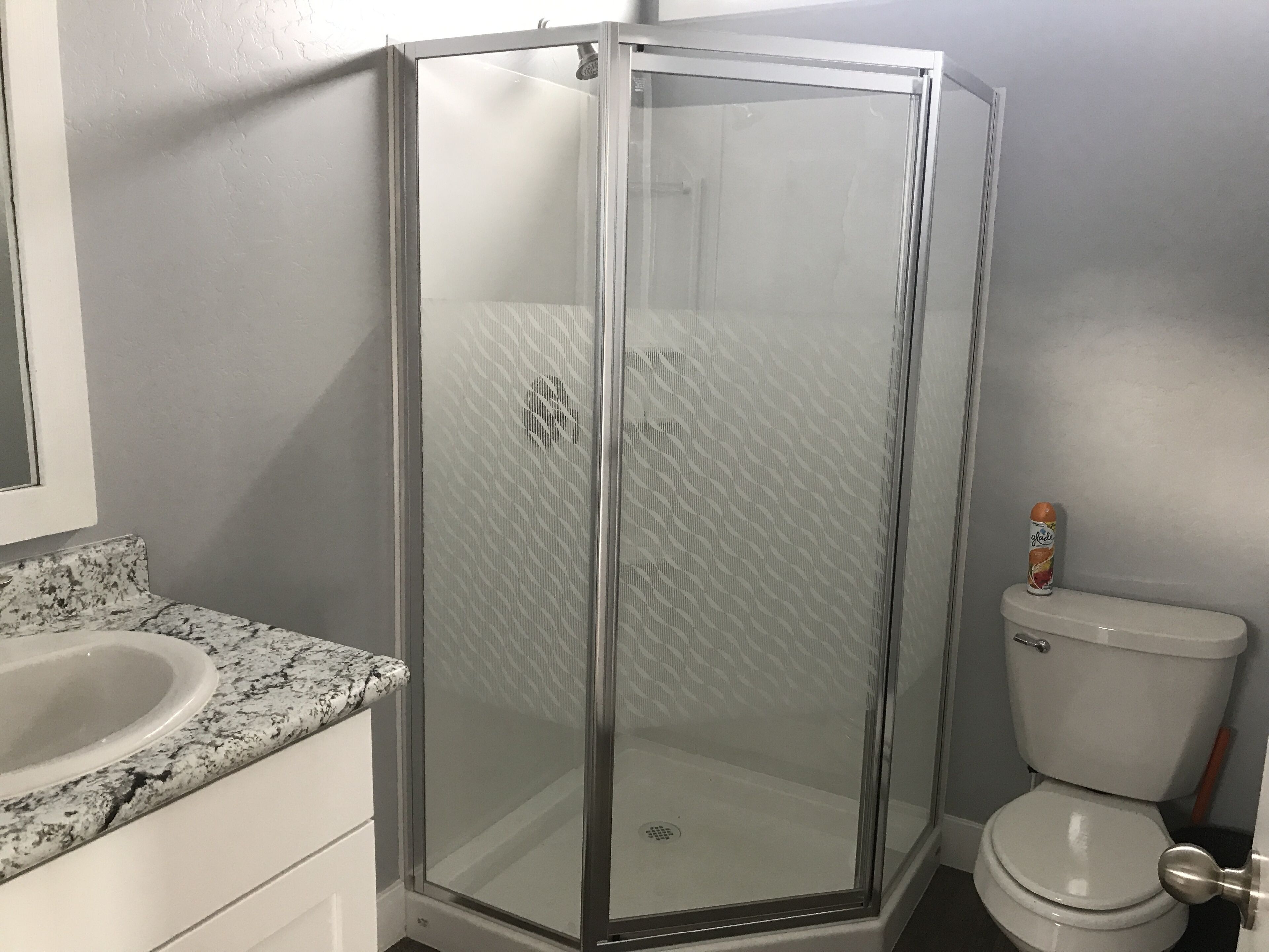 Ein Badezimmer mit einer Glaskabine zur Dusche, einer weißen Toilette und einem Waschbecken mit Granitplatte.