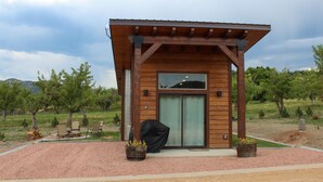 A modern wooden building with a covered patio area, outdoor seating, and potted plants. - Modern Tiny House in Apple Orchard w/Mountain View! Between Zion and Bryce (Glendale)