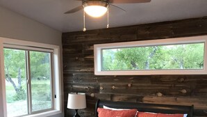 A bedroom with a bed, a ceiling fan, a window, and a nightstand. - Modern Tiny House in Apple Orchard w/Mountain View! Between Zion and Bryce (Glendale)