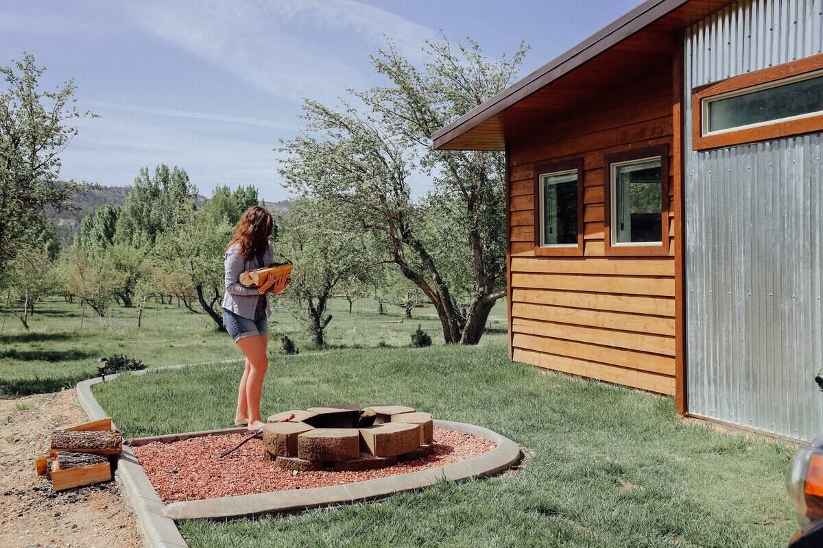 A wooden cabin with a fire pit in the yard, surrounded by trees.